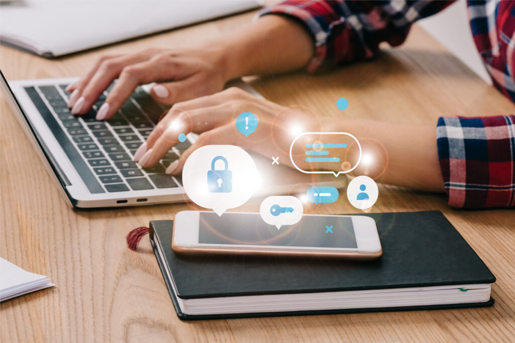 woman typing on her laptop; phone on a book with cybersecurity and managed IT services in Redwood City icons hovering above it